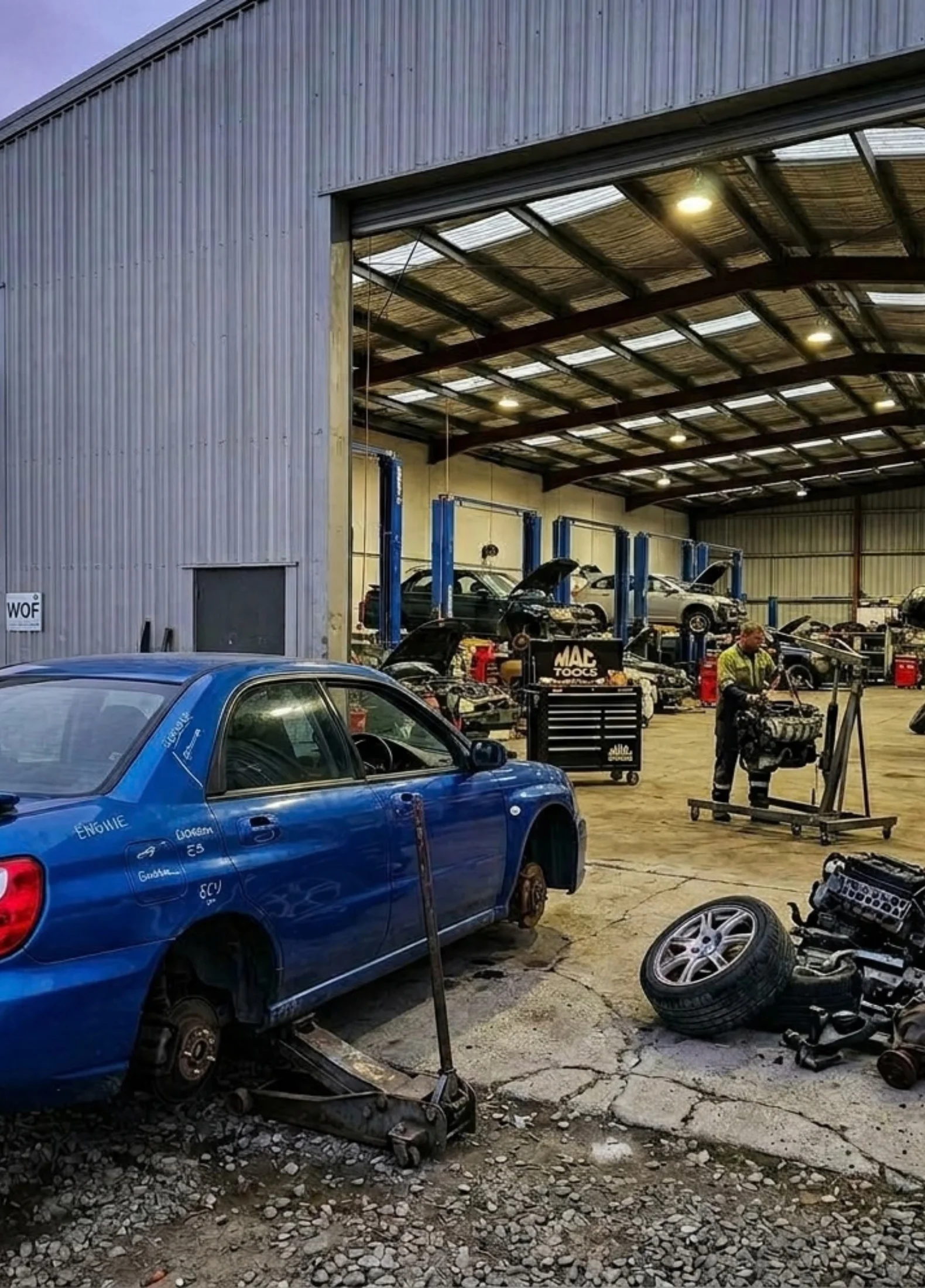 Car Wreckers Oamaru yard with mechanic dismantling vehicles.